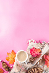 Autumn composition concept background. Cappuccino hot chocolate cup, with autumn bright leaves, pine cones, marshmallows, felt hat and blanket. Flatlay on pink trendy background, top view pattern