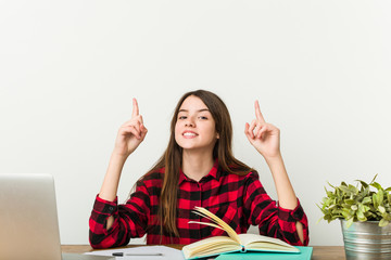 Young teenager going back to her routine doing homeworks indicates with both fore fingers up...
