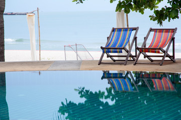 swimming pool and deck chair under coconut palm trees at the resort with beautiful sea view.