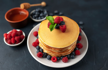 American pancakes with raspberries, fresh blueberries and honey. Healthy morning breakfast on concrete background