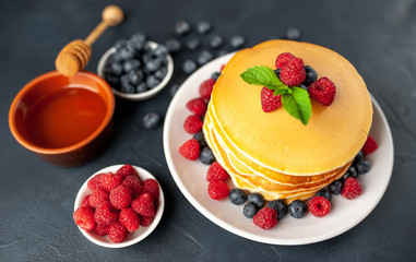 American pancakes with raspberries, fresh blueberries and honey. Healthy morning breakfast on concrete background