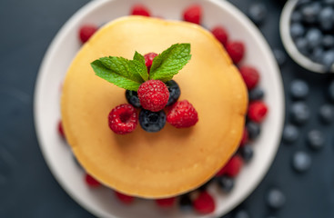 American pancakes with raspberries, fresh blueberries and honey. Healthy morning breakfast on concrete background