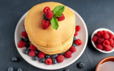 American pancakes with raspberries, fresh blueberries and honey. Healthy morning breakfast on concrete background