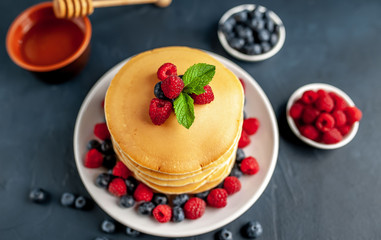 American pancakes with raspberries, fresh blueberries and honey. Healthy morning breakfast on concrete background