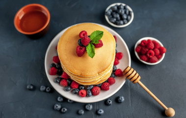 American pancakes with raspberries, fresh blueberries and honey. Healthy morning breakfast on concrete background