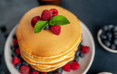 American pancakes with raspberries, fresh blueberries and honey. Healthy morning breakfast on concrete background