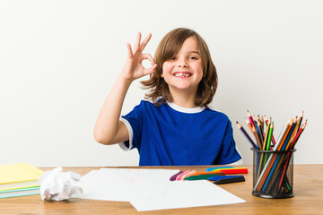 Little boy painting and doing homeworks on his desk cheerful and confident showing ok gesture.
