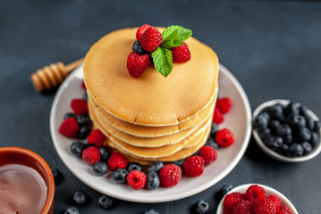 American pancakes with raspberries, fresh blueberries and honey. Healthy morning breakfast on concrete background