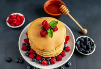 American pancakes with raspberries, fresh blueberries and honey. Healthy morning breakfast on concrete background