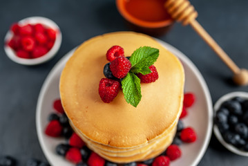 American pancakes with raspberries, fresh blueberries and honey. Healthy morning breakfast on concrete background