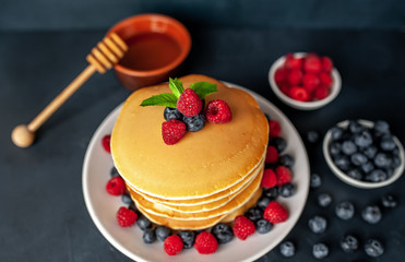 American pancakes with raspberries, fresh blueberries and honey. Healthy morning breakfast on concrete background
