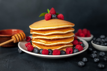 American pancakes with raspberries, fresh blueberries and honey. Healthy morning breakfast on concrete background