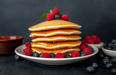 American pancakes with raspberries, fresh blueberries and honey. Healthy morning breakfast on concrete background