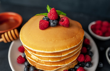 American pancakes with raspberries, fresh blueberries and honey. Healthy morning breakfast on concrete background