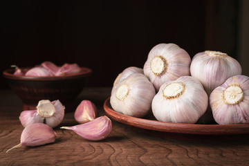 Heads of garlic in a ceramic dish and on a wooden table in rustic style