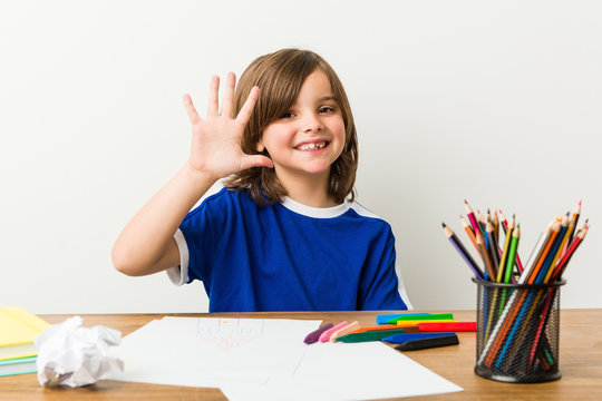 Little boy painting and doing homeworks on his desk smiling cheerful showing number five with fingers.