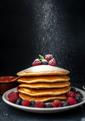 American pancakes with raspberries, fresh blueberries and honey. Healthy breakfast on concrete background, sprinkled with powdered sugar on pancakes