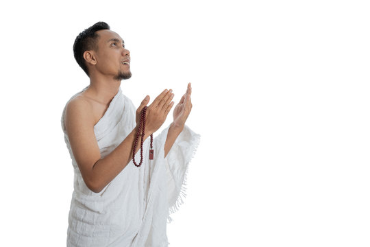 muslim asian man praying with prayer beads while standing in white traditional clothes