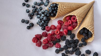 Top view of the three waffle cones from which poured on the table raspberries, currants, blackberries in powdered sugar