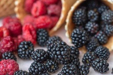 Raspberries, currants, blackberries close-up pour out of wafer cones, focus on blackberries
