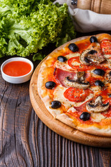 Pizza with tomato, olives, champignons, ham and cheese on round wooden plate
