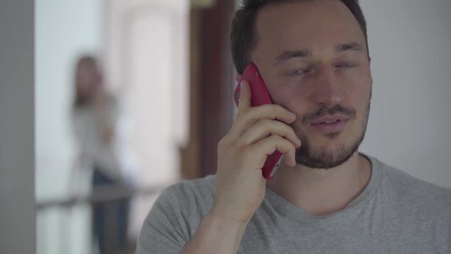 Portrait of happy man talking with his paramour by cellphone while his wife appears behind and overhearing the conversation. Family problems. Betrayal, mistrust, breakup concept. Focus on the woman.