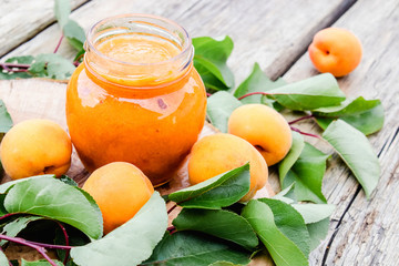 Homemade organic jam in a glass jar and ripe apricots on a wooden table.