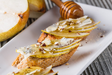 Appetizer bruschetta with pear, honey, walnut and blue cheese on white plate