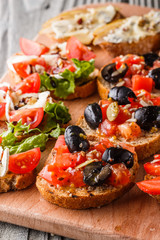 Assorted bruschetta with tomato, olives, camembert, blue cheese, lettuce, pear, honey on wooden board