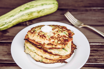 Fried zucchini pancakes stacked on plate, healthy organic summer food made with zucchini. Brown wood board background.