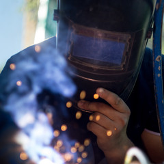 Worker in a protective mask in the process of metal welding
