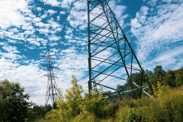 Extensive view of a tower with power lines for supply with energy; At a background the blue sky with open clouds which merge with foliage and the nature