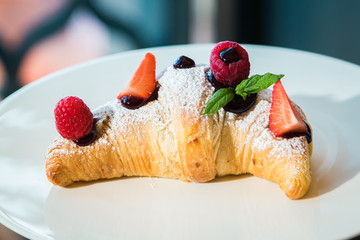 Croissant su piatto bianco con decorazioni di frutta, cioccolato e zucchero a velo