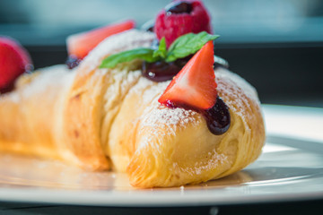 Croissant su piatto bianco con decorazioni di frutta, cioccolato e zucchero a velo