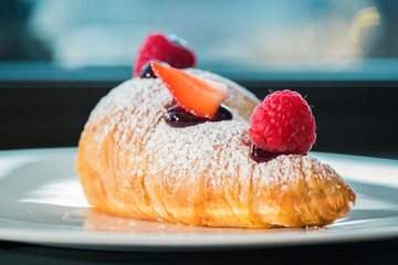 Croissant su piatto bianco con decorazioni di frutta, cioccolato e zucchero a velo