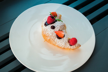 Croissant su piatto bianco con decorazioni di frutta, cioccolato e zucchero a velo