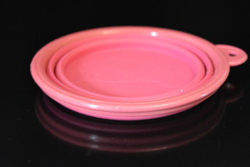Pink folding and multifunctional rubber plate, a bowl with a plastic edging on a black glossy surface.