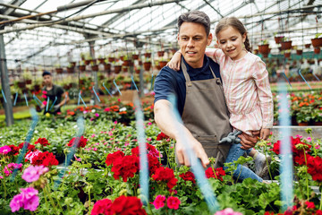 Happy father showing flowers to his small daughter in a greenhouse.