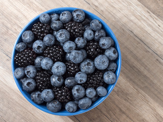 Bowl full of fresh blackberries and blueberries on a wooden background.