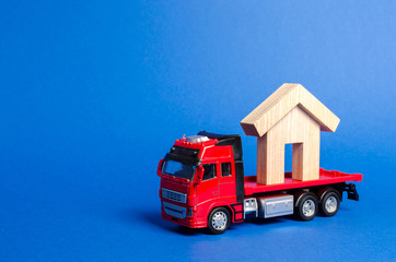 A red truck transports a wooden house. Concept of transportation and cargo shipping, moving company. Construction of new houses and objects. Industry. Logistics and supply. Move entire buildings.