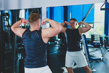 athlete in the gym looks in the mirror at his muscles