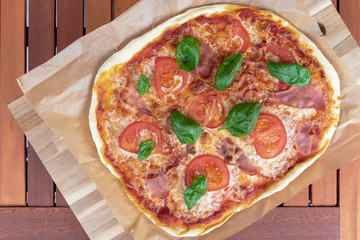 top view of fresh homemade pizza with serrano ham, sliced tomatoes and ham on wooden garden table