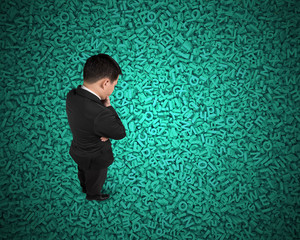 Big data concept, Thinking business man standing and looking at huge amount of 3d green concrete letters and numbers texture background.