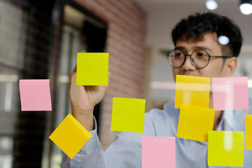 Young asian man writing on sticky note at office, business brainstorming creative ideas, office lifestyle, success in business concept