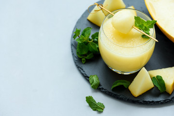 Cold fresh melon smoothie with melon ball and mint leaves on gray wooden background. Summer drink. Healthy food concept. Soft focus