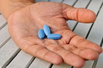 Hand of man holding blue pills. Closeup of a young man with a blue pills in one hand. Blue medicine pills. Medicine concept of viagra, medication for stomach, erection, sleeping, digestive, drugs