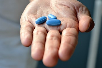 Hand of man holding blue pills. Closeup of a young man with a blue pills in one hand. Blue medicine pills. Medicine concept of viagra, medication for stomach, erection, sleeping, digestive, drugs  - obrazy, fototapety, plakaty