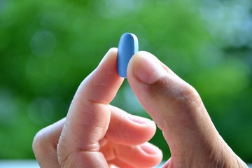 Hand of man holding blue pill. Closeup of a young man with a blue pill between  two fingers. Medicine pill. Medicine concept of viagra, medication for stomach, erection, sleeping, digestive, drugs 