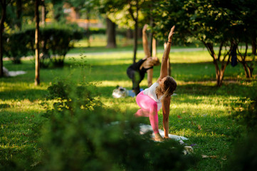 Two girls practice yoga in the park standing in the Revolved Triangle Pose