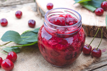 Fresh cherry jelly with fruit on a wooden background near the berries and green leaves.